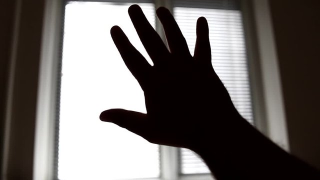 Close-up silhouette of a man's hand reaching for the light against the background of a window in the room. Hand silhouette raised up to the light.