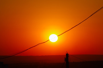 The disc of the sun crossed by an electricity line in orange sky at sunset golden hour