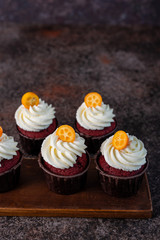 Red velvet cupcakes with white cream on top decorated with kumquat slice.
