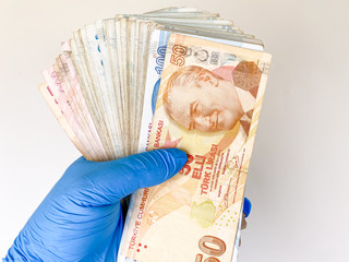 a close-up of a man's hand in rubber disposable blue gloves holding turkish liras. Coronavirus...