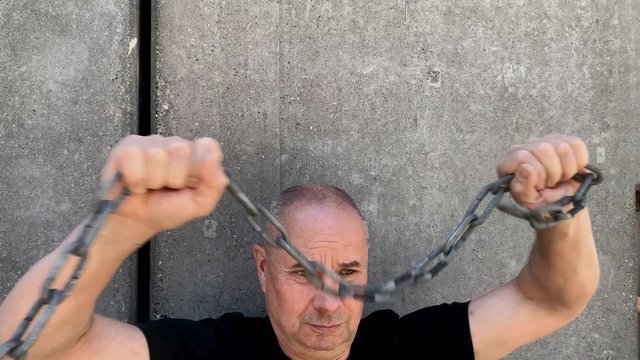 strong man holds thick iron chains in his hands, yanks them, tries to break the steel, the concept of strength, fetters, bondage, conclusions