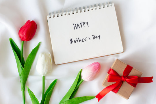 Write text happy mother's day on paper notebook with tulips flowers on white background.