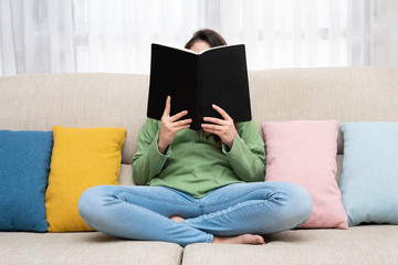 Girl sitting on a center of couch reading a book