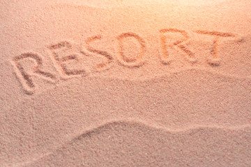 Fototapeta na wymiar RESORT lettering on sand with wave and evening light. Minimal exotic vacation and travel concept, Flat lay top view copy space