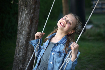 Portrait of a 10 year old schoolgirl with long londe hair and jeans jacket on a swing smiling at the camera