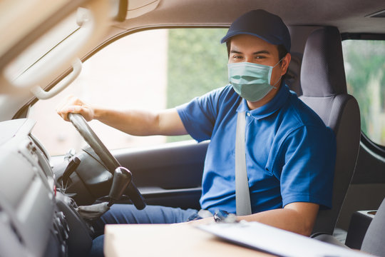 Young asian delivery man wearing protective face mask driving his van with packages on the front seat due to Coronavirus disease or COVID-19 outbreak situation in all of landmass in the world.