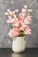 Pink flower in vase on black table on gray background. Close up