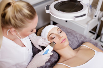 cosmetology and beauty concept - female cosmetologist doing ultrasound facial peeling procedure