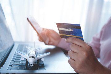 Tourist is booking plane tickets online using a credit card on the website agency in order to travel around the world. The concept is travel, tourism and online ticket payment through mobile app.