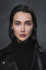 Fototapeta na wymiar Beautiful young brunette girl in a black sweater and black leather jacket on a gray background.
