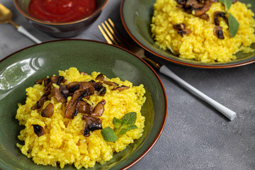 Italian risotto with champignons and parmesan on a gray background in dark plates. Rice is seasoned with turmeric and herbs.