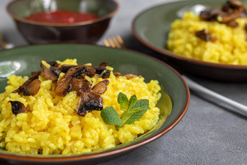 Italian risotto with champignons and parmesan on a gray background in dark plates. Rice is seasoned with turmeric and herbs.
