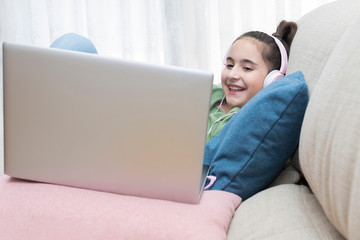 Girl on a couch with a laptop and headphones while smiling