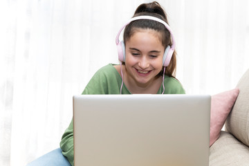 Girl sitting on a couch using a laptop with headphones while smiling