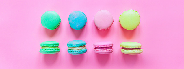 Sweet almond colorful pink blue yellow green macaron or macaroon dessert cake isolated on trendy pink pastel background. French sweet cookie. Minimal food bakery concept. Flat lay top view banner