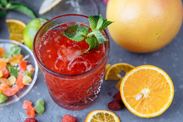 Fresh pink lemonade with raspberries decorated with mint leaves, orange, lime and candied fruit on a decorative background