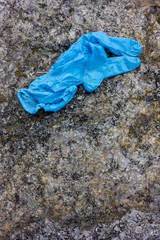 Used medical gloves on the stone. Blue crumpled disposable glove dumped on the ground pose public health risks and pollute the environment