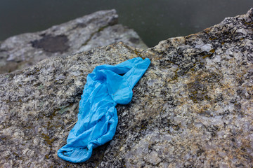 Used medical gloves on the stone. Blue crumpled disposable glove dumped on the ground pose public health risks and pollute the environment