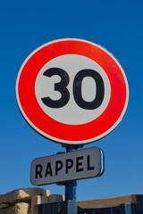 traffic sign with a speed limit of 30 and the French word for remember against blue sky