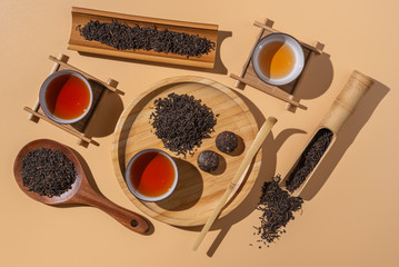 Tea ceremony in minimalism style, black puer tea in ceramics bowls,dry pu-erh tea leaves in a wooden bamboo spoons and plate on a beige background.