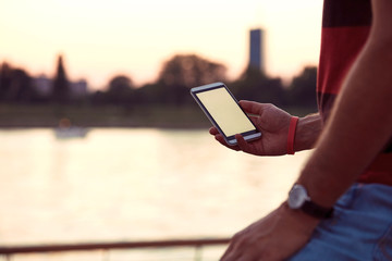 Man holding cellphone near river.
