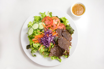 vegetable salad top with grilled sliced beef in white plate served dressing in a dipping bowl on isolated white background