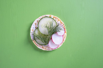 on a green table lies a corn waffle and on it a cucumber, radish and dill