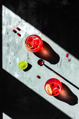 Cranberry tonic with lime in beautiful glasses, grey background, direct natural light, top view photo