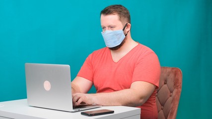 Side view portrait of a cheerful brunette man with surgical medical mask working on email laptop typing or chatting in social.