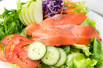vegetable salad top with smoked salmon and sliced green apple on a white plate