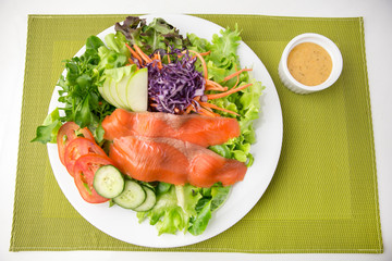 vegetable salad top with smoked salmon and sliced green apple on a white plate on green placemat