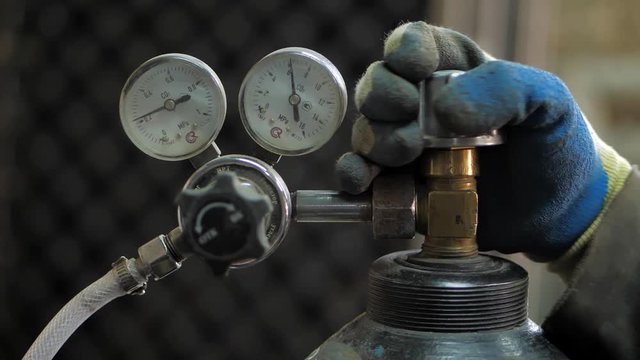 In the workshop. Close-up. The man opens an oxygen cylinder for welding