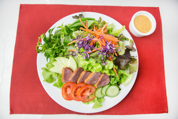 vegetable salad top with sliced roasted duck in white plate on red placemat