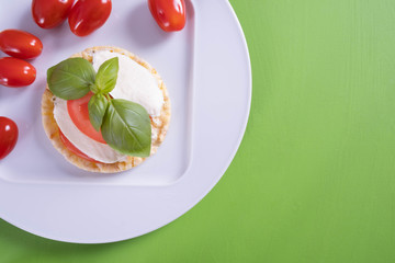 on a white plate lies a corn wafer and on it mozzarella, tomato and basil