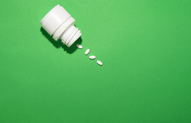 the jar of medicines is on a green background, some pills have fallen out