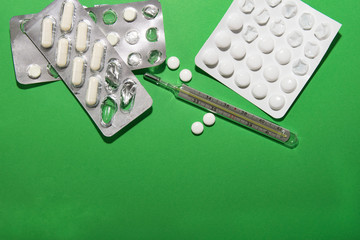 Packs of pills and a thermometer lie on a green background, next to them are several tablets...