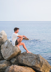 Young caucasian man sitting on a stone pier in the sea