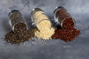 Chia, flax and sesame seeds in a glass bowl contain healthy vitamins and minerals. On a gray background under concrete.