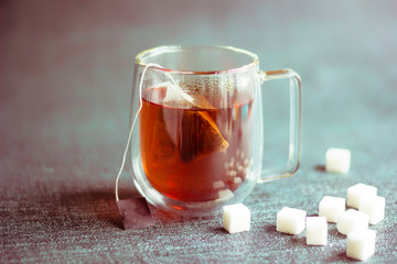 Glass transparent Cup with double walls and brewed tea and a bag in the Cup. sugar in refined cubes is scattered nearby. Toned. Copy space