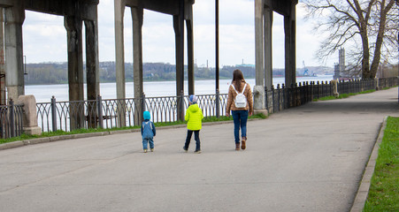 A mother and two small children walk along the embankment on a clear spring day