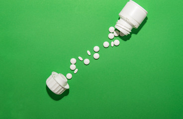 white pills lie on a green background with a jar