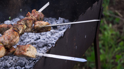 Cooking barbecue on the mangal in nature. Traditional Russian shashlik on a barbecue skewer on sunny yard background. Grilled tasty meet cooking on the party.