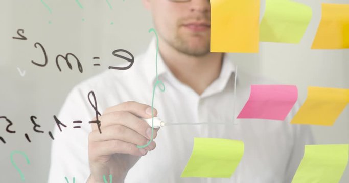 Man draws graph with arrows on transparent screen near stickers with notes and formulas. Einstein's theory of relativity. Science and education concept. Learning new ideas or hypothesis at University.