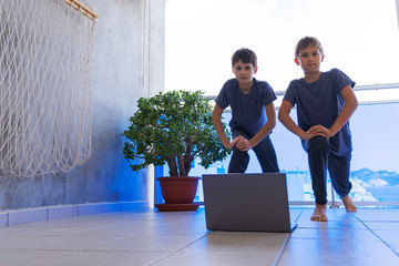 Children with laptop computer doing sport exercises at home on balcony. Sport, healhty lifestyle, active leisure, stay at home, online learning, online training