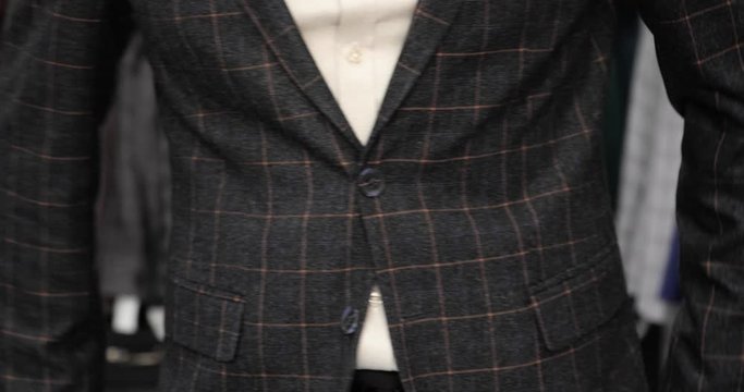 Man is fastening suit jacket trying it in clothing store, hands closeup. Young businessman guy is choosing and buying elegant costume, front view.