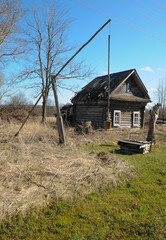 abandoned old house in a Russian village on a Sunny day, dry grass around the house, old well type "crane" early spring