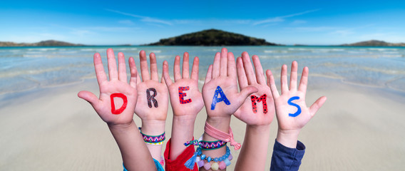 Children Hands Building Colorful English Word Dreams. Ocean And Beach As Background