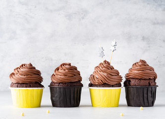 Chocolate cupcakes in yellow paper cups with chocolate creamy frosting (made of cottage cheese and whipped heavy cream) and blue stars on grey and white concrete background. Copy space, close up view.