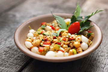 Chickpea salad with colorful vegetables and marinated onions.
Salad, a side dish served in a stoneware bowl. Dish on a wooden background.
