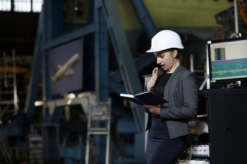 Portrait of a female factory manager in a white hard hat and business suit. Controlling the work process at the airplane manufacturer.
